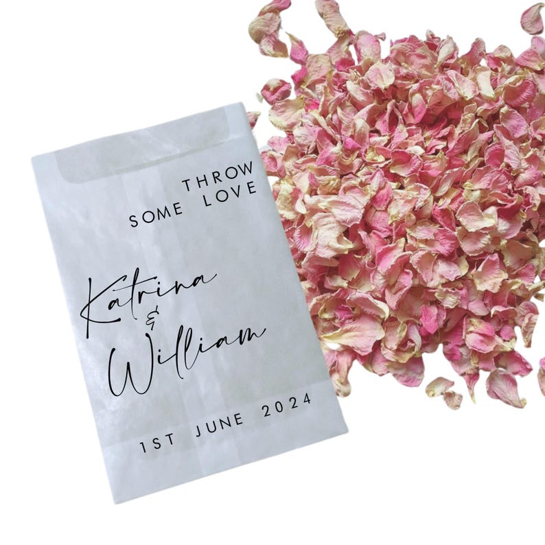 May include: White paper bag with the text "Throw Some Love" and "Katrina & William" with the date "1st June 2024". The bag is filled with pink rose petals.