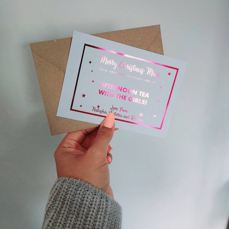 May include: A white card with a pink foil border and stars. The text on the card reads "Merry Christmas Mum, this voucher entitles you to Afternoon Tea with the Girls! Love from Natasha, Victoria and Ru"