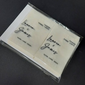 May include: A stack of white tissue paper favors with black text that reads "Lauren & James" and "Some Throw Love" with the date "24th June 2022".