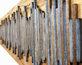 May include: A wooden wall art piece with a wave-like pattern made of vertical wooden and metal strips. The wood is a light brown color and the metal strips are a dark gray color.