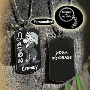 Peut inclure: Un collier avec une médaille en métal noir et une chaîne argentée. Le devant de la médaille présente une image de dessin animé de Grumpy de Blanche-Neige et les Sept Nains et le nom "Jason" écrit verticalement. Le dos de la médaille porte les mots "Votre message" écrits en blanc. La médaille peut être personnalisée avec un nom et un message.