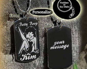 Puede incluir: Collar o llavero de metal negro en forma de placa de identificación para perro con una cadena plateada. La parte delantera presenta una imagen en blanco y negro de Betty Boop con el texto "Betty Boop" y "Kim". La parte trasera está en blanco con el texto "tu mensaje".
