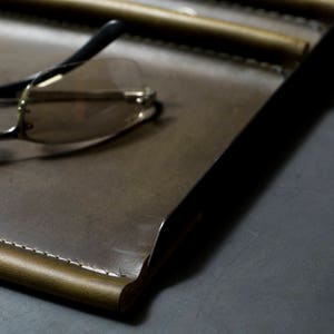 May include: A brown leather tray with a stitched edge and a pair of eyeglasses on top.