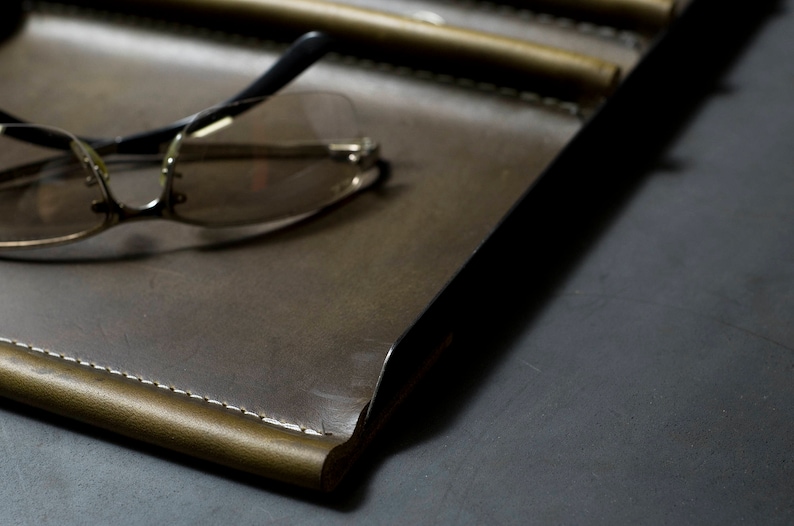 May include: A brown leather tray with a stitched edge and a pair of eyeglasses on top.