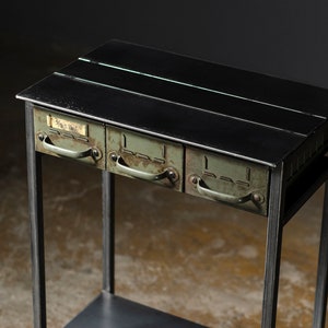 May include: A black metal side table with three drawers. The drawers are painted a light green color and have metal handles. The table has a black metal shelf underneath the drawers.