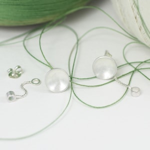 May include: A pair of silver earrings with a round, slightly domed shape. The earrings are connected to a small silver chain with a round bead at the end.