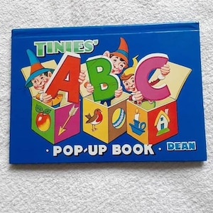 May include: A blue pop-up book titled "Tinies' ABC" with colourful illustrations of characters holding letters in boxes. The book is by Dean.
