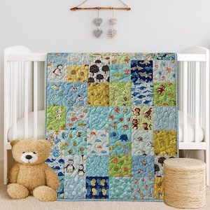 May include: A patchwork quilt featuring a variety of square fabric panels with colorful illustrations of animals, butterflies, and trees in shades of blue, green, and yellow. The quilt is draped over a white crib, with a tan teddy bear nearby.