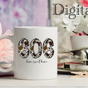 May include: White ceramic mug with a brown and white cow print design featuring the number "606" and the text "home sweet home".