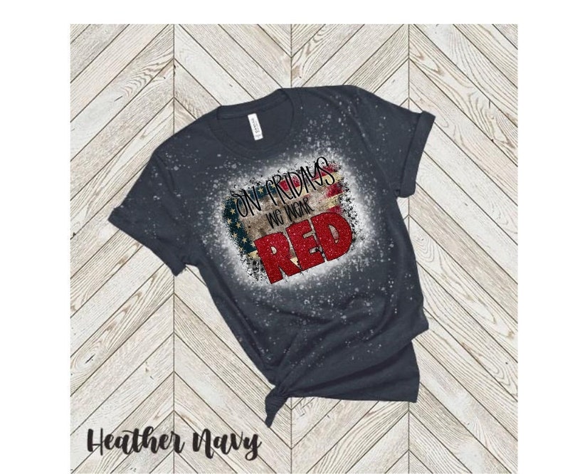 Może przedstawiać: Koszulka w kolorze ciemnego hebanowego granatu z przetartym wzorem amerykańskiej flagi i napisem "On Fridays We Wear Red".
