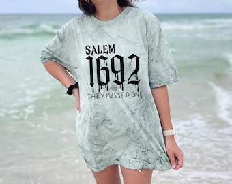 May include: A light green tie-dye t-shirt with black text that reads "Salem 1692 They Missed One".