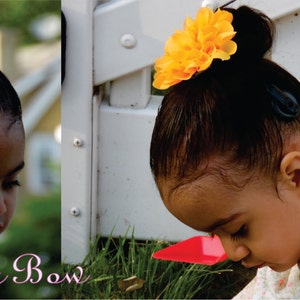 May include: A young girl with dark hair wearing a white and pink floral dress with a yellow flower hair clip. The girl is looking down at something off camera.