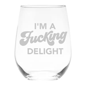 May include: A clear stemless wine glass with the text "I'M A Fucking DELIGHT" in gray lettering. The glass has a rounded shape and is designed for wine.