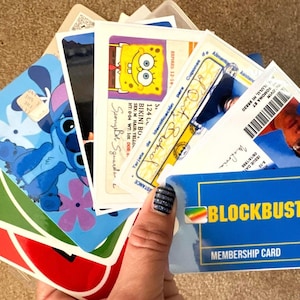 May include: A collection of cards and stickers featuring various characters, including Stitch, SpongeBob SquarePants, and a Blockbuster membership card. The cards are arranged in a fan shape, with the Blockbuster card at the bottom.