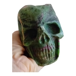 May include: A green and pink skull sculpture carved from stone. The skull is detailed and has a realistic appearance.