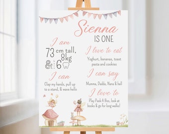 Puede incluir: Un cartel imprimible rosa y blanco con el nombre Sienna y el texto "IS ONE". El cartel incluye detalles sobre la edad, la altura, el peso y las actividades favoritas del niño. El cartel está decorado con una ilustración de hada y hongo.