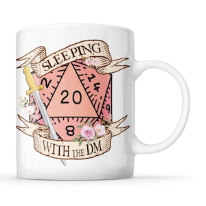 May include: White ceramic mug with a pink D20 die design, a golden sword, and floral details. The mug displays the text "SLEEPING WITH THE DM" on a banner. A great gift for Dungeons and Dragons enthusiasts.