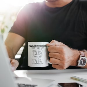 Puede incluir: Taza de cer&aacute;mica blanca con el texto "PROGRAMMERS WHILE CODING" y una ilustraci&oacute;n humor&iacute;stica de la experiencia de un programador. La taza tiene un asa y la sostiene una persona.