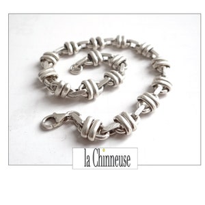 May include: A silver chain bracelet with a unique interwoven design. The bracelet has a lobster claw clasp.