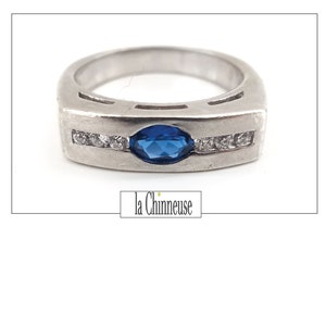 Peut inclure: Une bague en argent avec une pierre précieuse bleue et une rangée de pierres précieuses claires.
