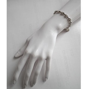 May include: A silver bracelet with a twisted chain design. The bracelet is on a white mannequin hand.