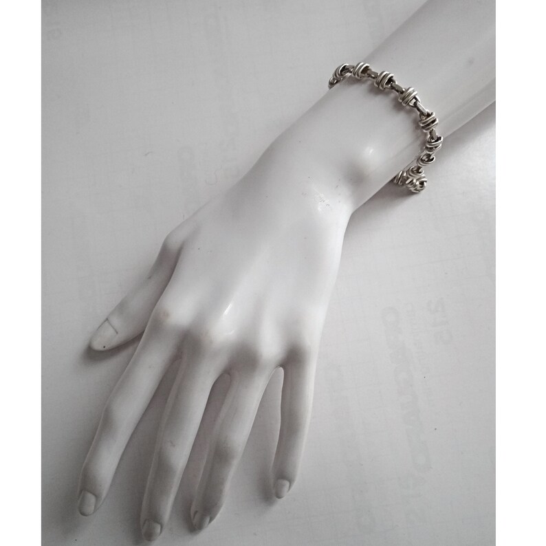 May include: A silver bracelet with a twisted chain design. The bracelet is on a white mannequin hand.