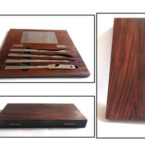 Peut inclure: Un ensemble de quatre outils en argent dans une bo&icirc;te en bois avec un grain de bois fonc&eacute;. Les outils sont dispos&eacute;s en rang&eacute;e et ont tous la m&ecirc;me longueur. La bo&icirc;te a un couvercle &agrave; charni&egrave;res et une petite plaque m&eacute;tallique &agrave; l'int&eacute;rieur.
