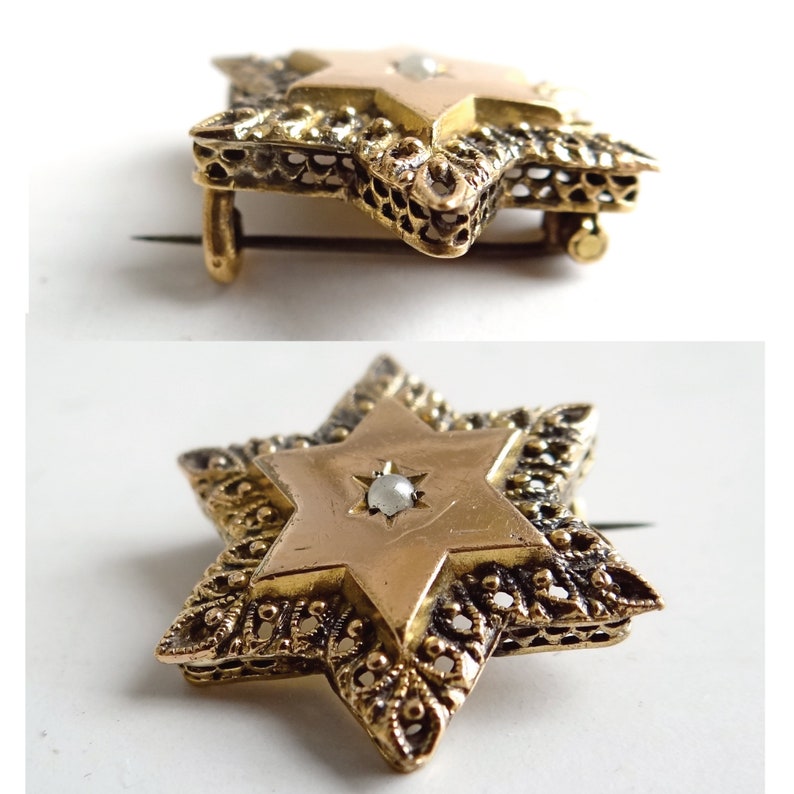 Op de afbeelding: Een gouden Davidster-broche met een parel in het midden. De ster is omgeven door een delicaat filigraan ontwerp.
