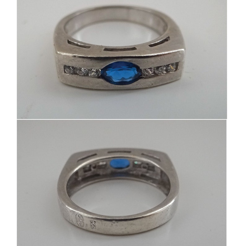 Op de afbeelding: Een zilveren ring met een blauwe ovale edelsteen en een rij heldere edelstenen. De ring is gemarkeerd met "925" aan de binnenkant.