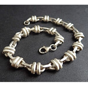 May include: A silver chain bracelet with a unique knot design. The bracelet has a lobster clasp closure.