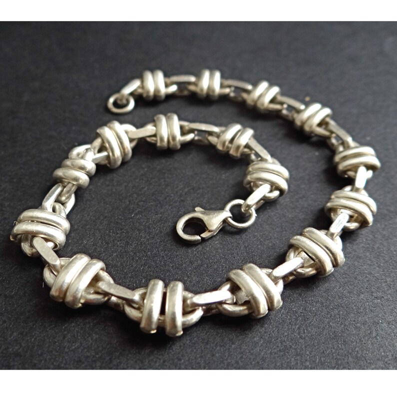 May include: A silver chain bracelet with a unique knot design. The bracelet has a lobster clasp closure.