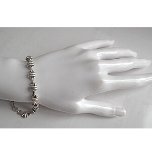 May include: A silver bracelet with a chain link design. The bracelet is made of small, round links that are connected together in a repeating pattern.