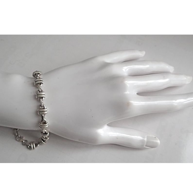 May include: A silver bracelet with a chain link design. The bracelet is made of small, round links that are connected together in a repeating pattern.