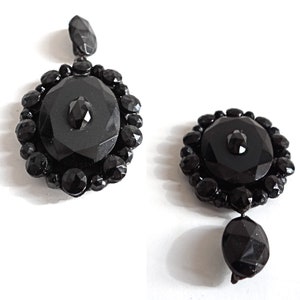 May include: A pair of black glass earrings with a round, faceted design. Each earring features a large, round, black glass stone surrounded by smaller, faceted black glass stones.