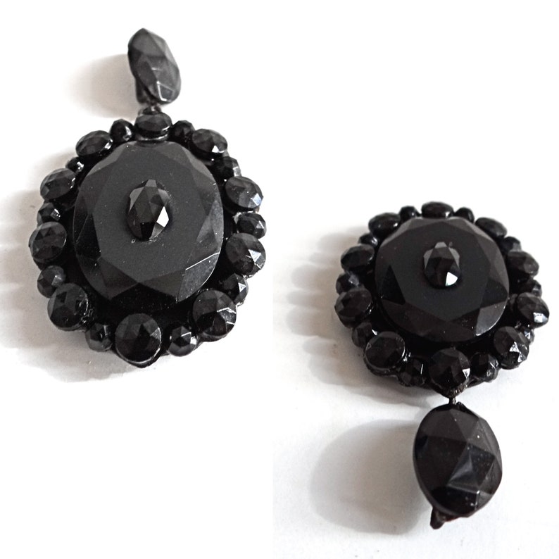 May include: A pair of black glass earrings with a round, faceted design. Each earring features a large, round, black glass stone surrounded by smaller, faceted black glass stones.