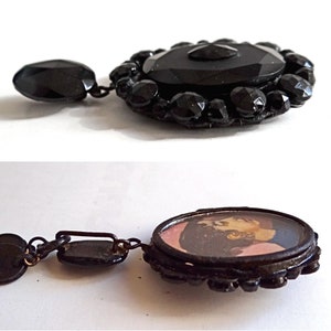 May include: A black glass cameo pendant with a black jet bead border. The cameo features a portrait of a woman with dark hair and a pink dress.