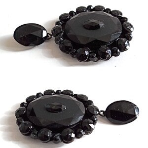May include: A pair of black glass earrings with a large, faceted, oval-shaped center piece surrounded by smaller, faceted black glass beads. The earrings have a dangling drop.