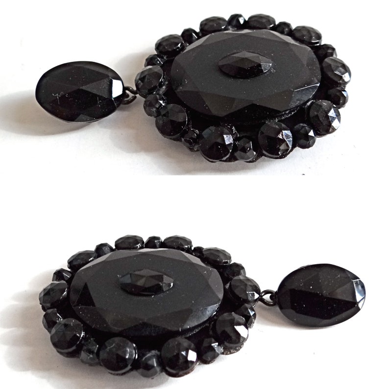 May include: A pair of black glass earrings with a large, faceted, oval-shaped center piece surrounded by smaller, faceted black glass beads. The earrings have a dangling drop.