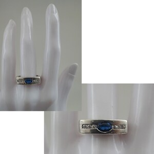 Op de afbeelding: Een zilveren ring met een blauwe ovale edelsteen en kleinere heldere edelstenen gezet in een band.