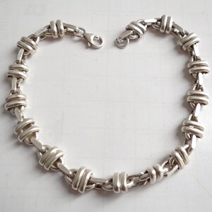 May include: A silver chain bracelet with a unique, interwoven design. The links are thick and have a polished finish.