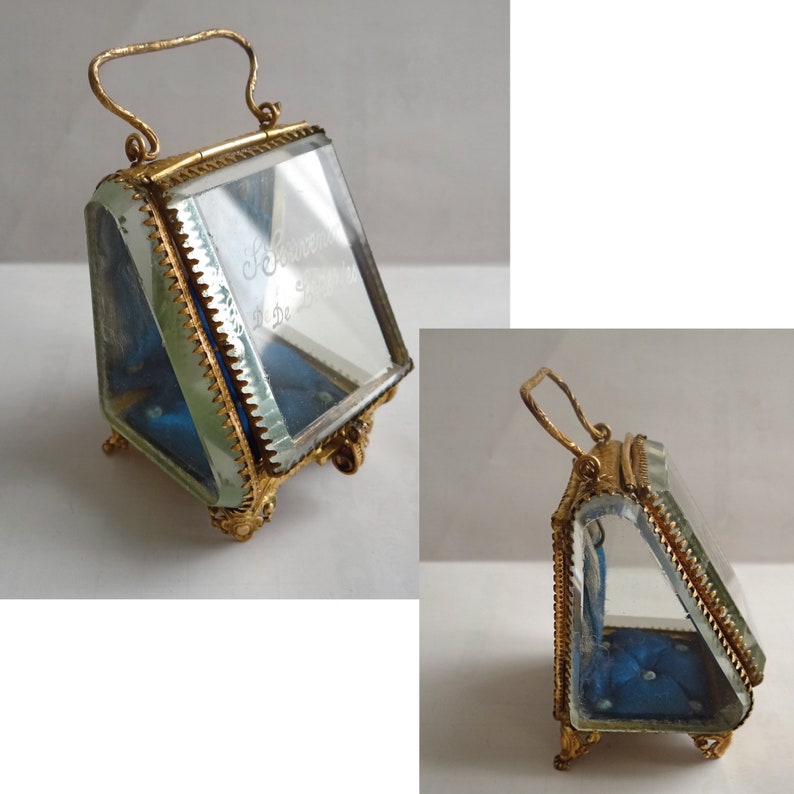 Op de afbeelding: Een kleine, goudkleurige glazen vitrine met een scharnierend deksel en een handvat. De vitrine heeft een blauwe fluwelen binnenkant en staat op vier kleine pootjes. Het glas is gegraveerd met de tekst "Souvenir de Paris 22 Decembre".