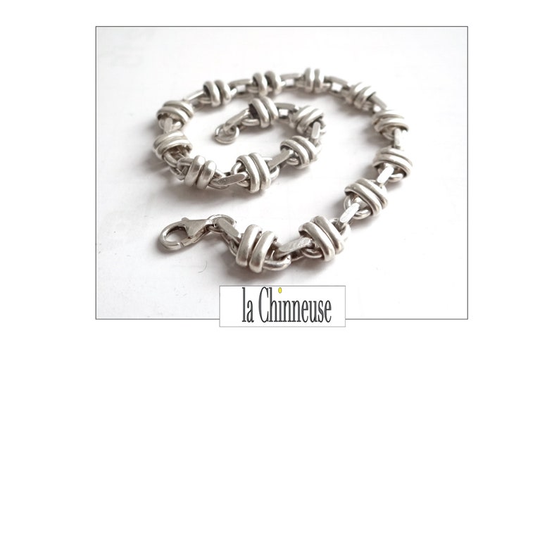 May include: A silver chain bracelet with a unique interwoven design. The bracelet has a lobster claw clasp.