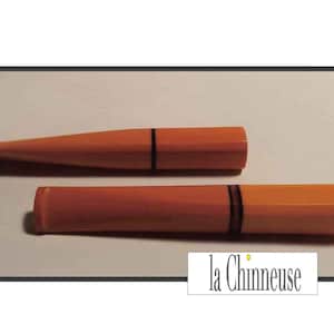 May include: Two orange and black cigarette holders. The holders are made of a smooth, hard plastic. The top of the holders are rounded and the bottom is flat. The holders are approximately 15 cm long.