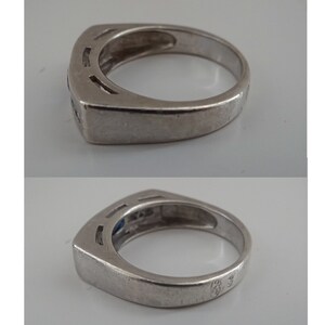 Op de afbeelding: Een zilveren ring met een blauwe edelsteen en een vierkante zetting. De ring heeft een band met een getextureerd ontwerp en een keurmerk aan de binnenkant.