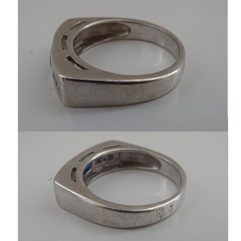 Op de afbeelding: Een zilveren ring met een blauwe edelsteen en een vierkante zetting. De ring heeft een band met een getextureerd ontwerp en een keurmerk aan de binnenkant.