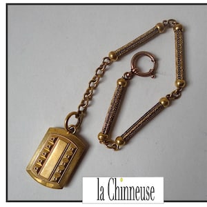 May include: A gold pocket watch chain with a rectangular pendant. The chain is made of a woven design and has a spring ring clasp. The pendant has a decorative design with a blank space in the center.