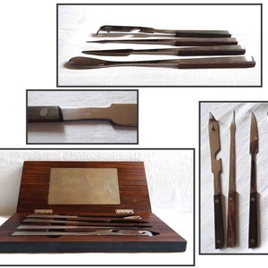 Peut inclure: Un ensemble de sept outils en acier inoxydable avec des manches en bois, dans une bo&icirc;te en bois. Les outils comprennent une cuill&egrave;re, un couteau, une fourchette et quatre autres outils.