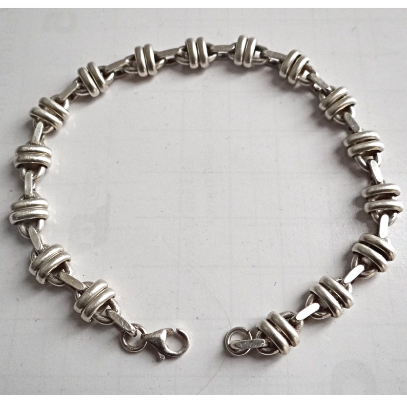 May include: A silver bracelet with a chain link design. The links are twisted and have a rounded shape.