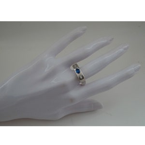 Op de afbeelding: Een zilveren ring met een blauwe edelsteen en kleinere heldere edelstenen die in de band zijn gezet.