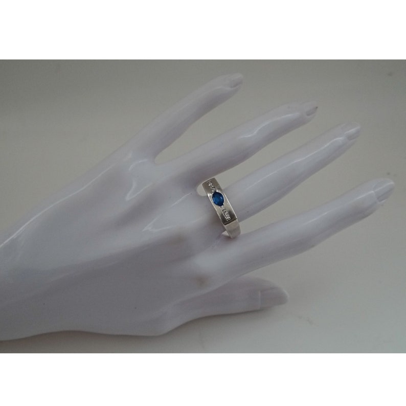 Op de afbeelding: Een zilveren ring met een blauwe edelsteen en kleinere heldere edelstenen die in de band zijn gezet.